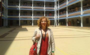 fiona moore stood in front of a building,wearing red dress, grey over jacket and holding a red bag.