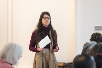 Dr Marina Pérez de Arcos stood giving a talk with a piece of paper in her hand, wearing a burgundy top and grey blouse. 