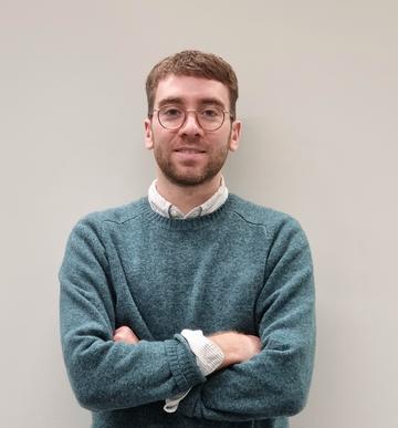 Andrew Creagh stood by grey background, arms folded. 