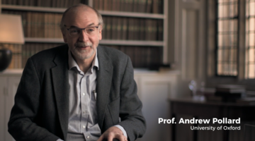 screenshot of Professor Andrew Pollard, sat on left wearing suit jacket and open shirt with books in the background.