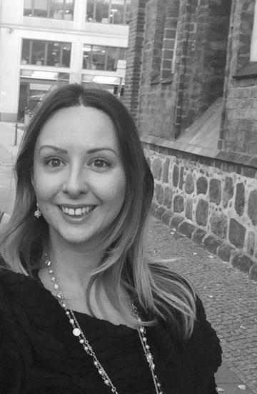 Lana Pasic head and shoulders shot in black and white, smiling, on a side street with brickwork behind.