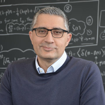 Image of Ramin Golestanian seated in front of a blackboard filled with mathematical calculations