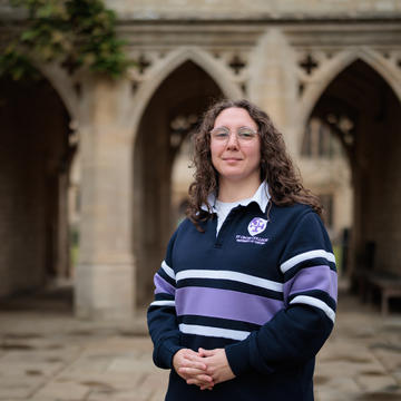 Jessica De Marco stands in front of the college arches, wearing a purple striped St Cross rugby shirt.
