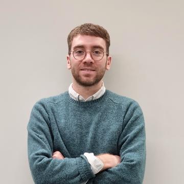 Andrew Creagh stood by grey background, arms folded. 