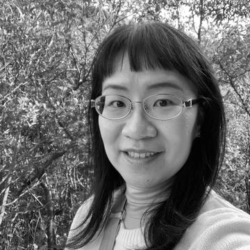 black and white head and shoulders shot of Flora Lau, wearing glasses and trees in the background.