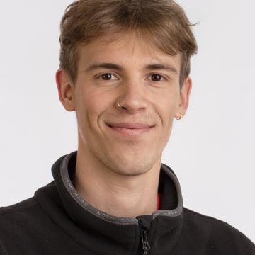 Jacques Bouvier head and shoulders shot, smiling with, short brown hair, nose piercing and wearing zip up top.