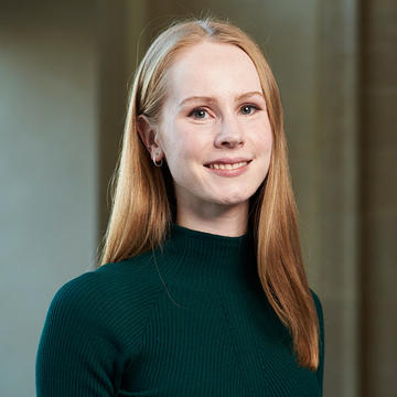 Emma Copland has long blonde hair, and wear a dark turtleneck top