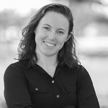 black and white shot of Vanessa Gerber, smiling, long brown hair and wearing an open shirt.