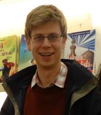 matthew woolgar head and shoulders shot, wearing glasses, open jacket, red pullover and shirt.