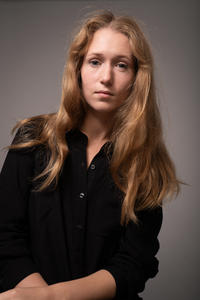 nadezhda kamenkovich profile shot, long hair, wearing dark shirt on a grey background