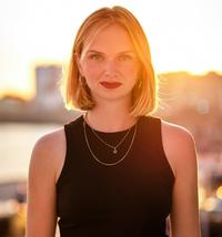 Kristina Lunz head and shoulders in black dress with sunkissed background 