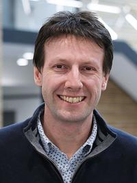 head and shoulders shot of daniel wilson, smiling wearing an open shirt and pullover.