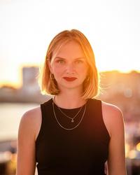 Kristina Lunz head and shoulders in black dress with sunkissed background 